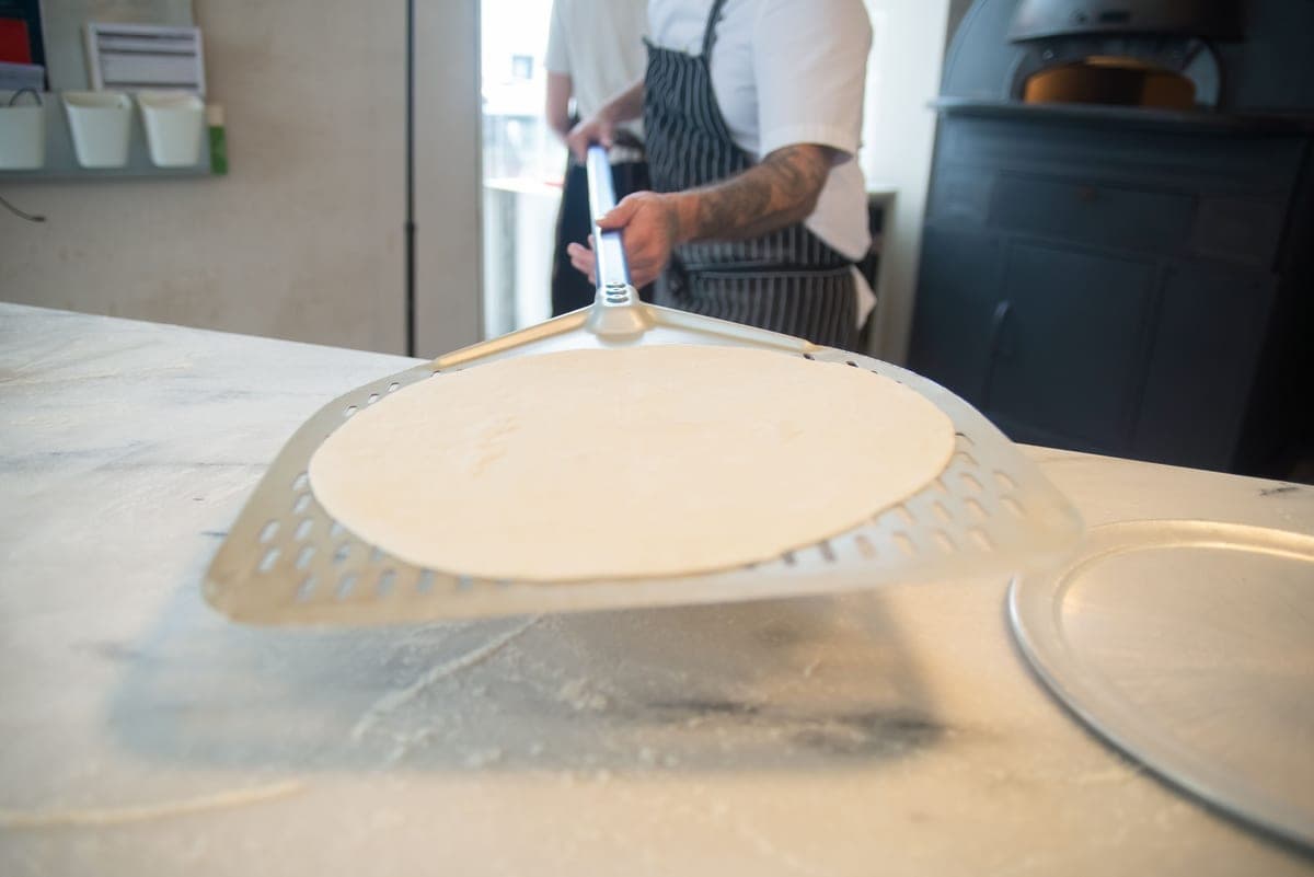 Pizza dough balls and a wooden peel on a floured surface