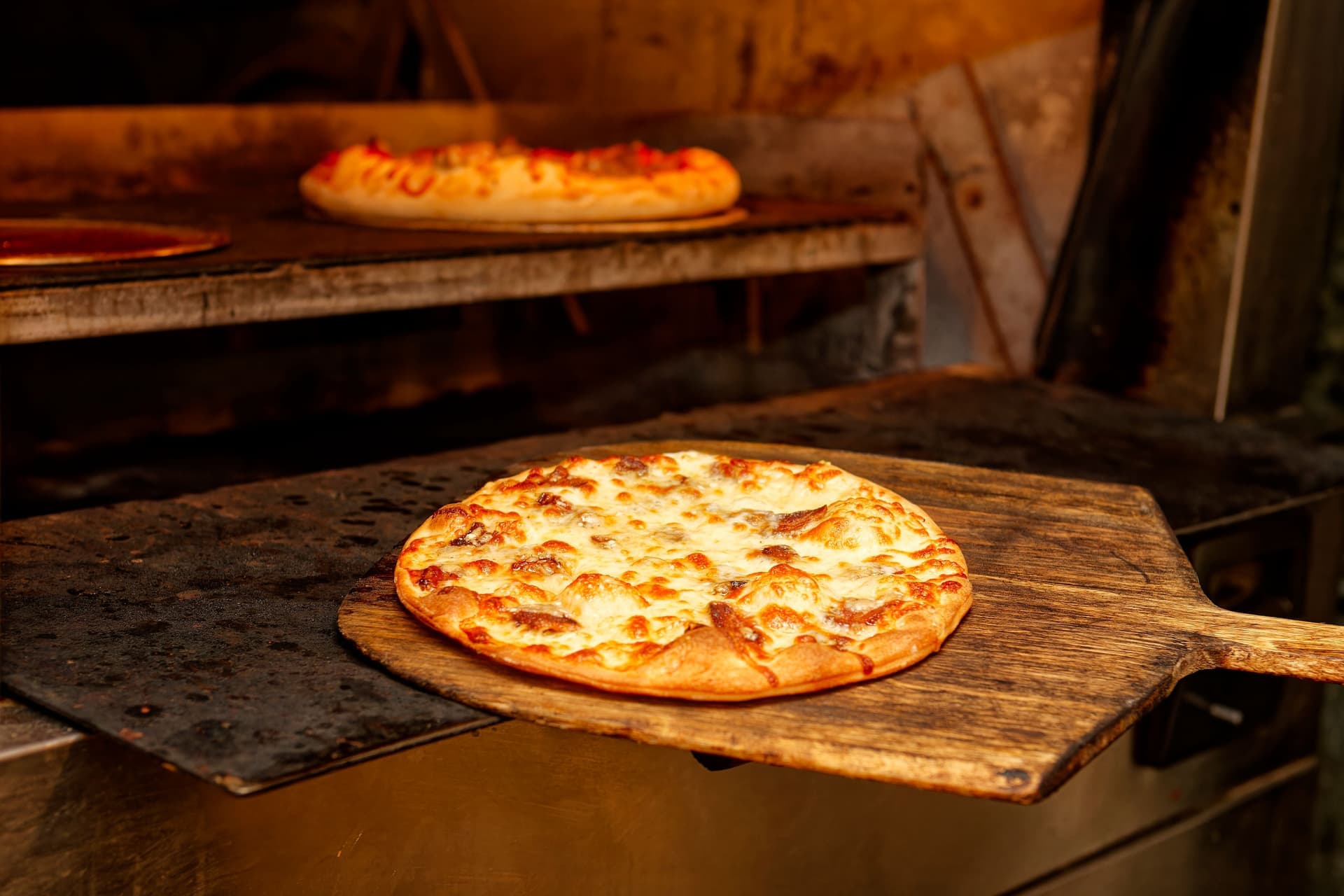 A pizza on a wooden peel beside an oven