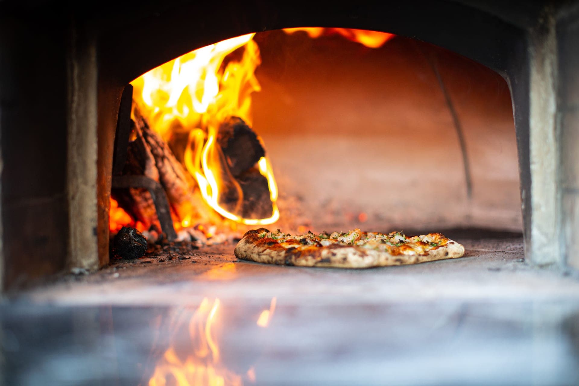 A pizza baking inside a wood-fired oven
