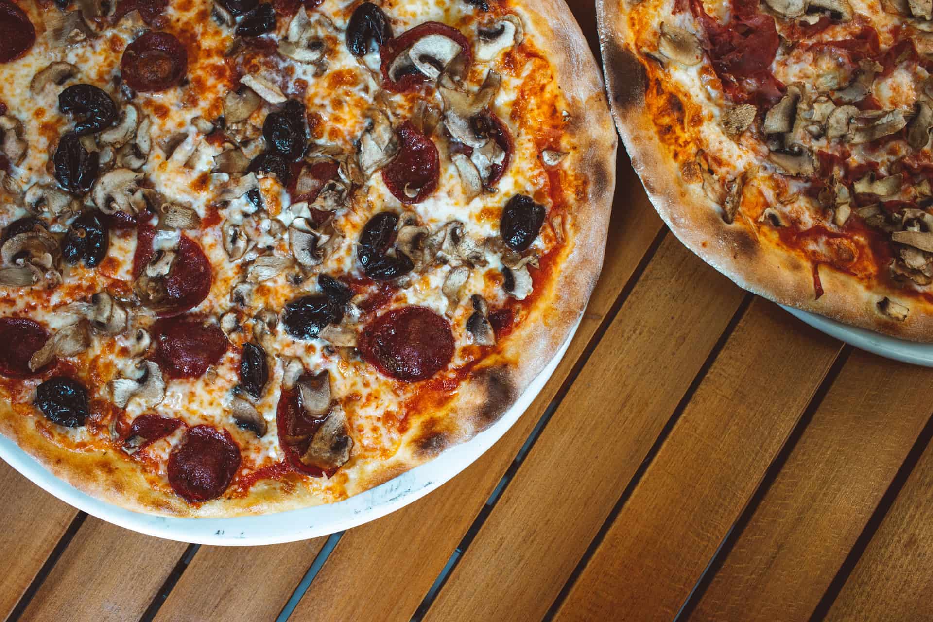 Two finished pizzas of different sizes side by side on a wooden table