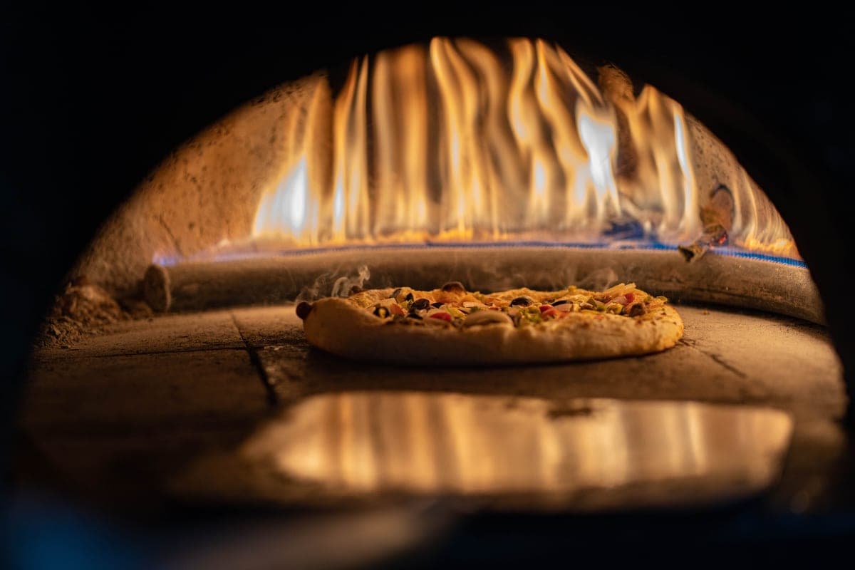 A pizza cooking inside a hot oven with flames above