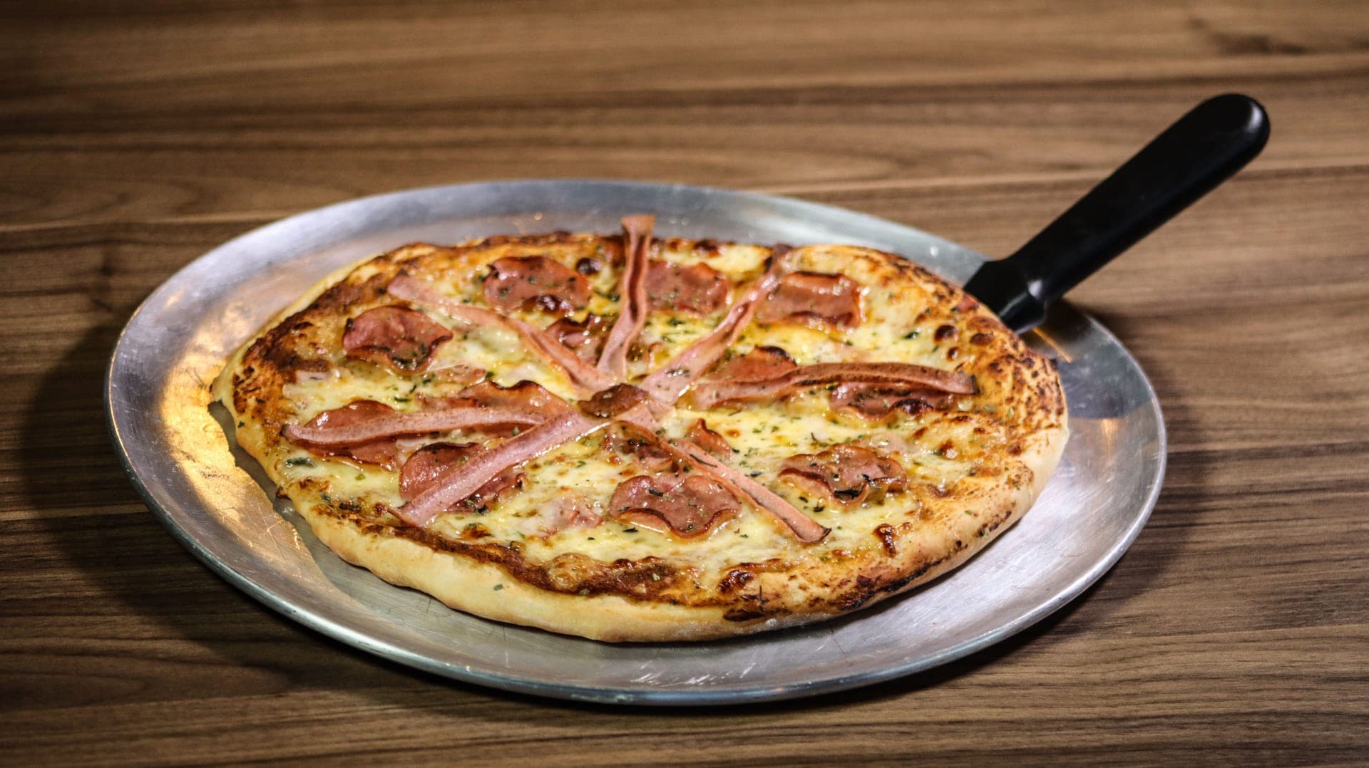 A baked pizza resting on a bare aluminum pizza pan