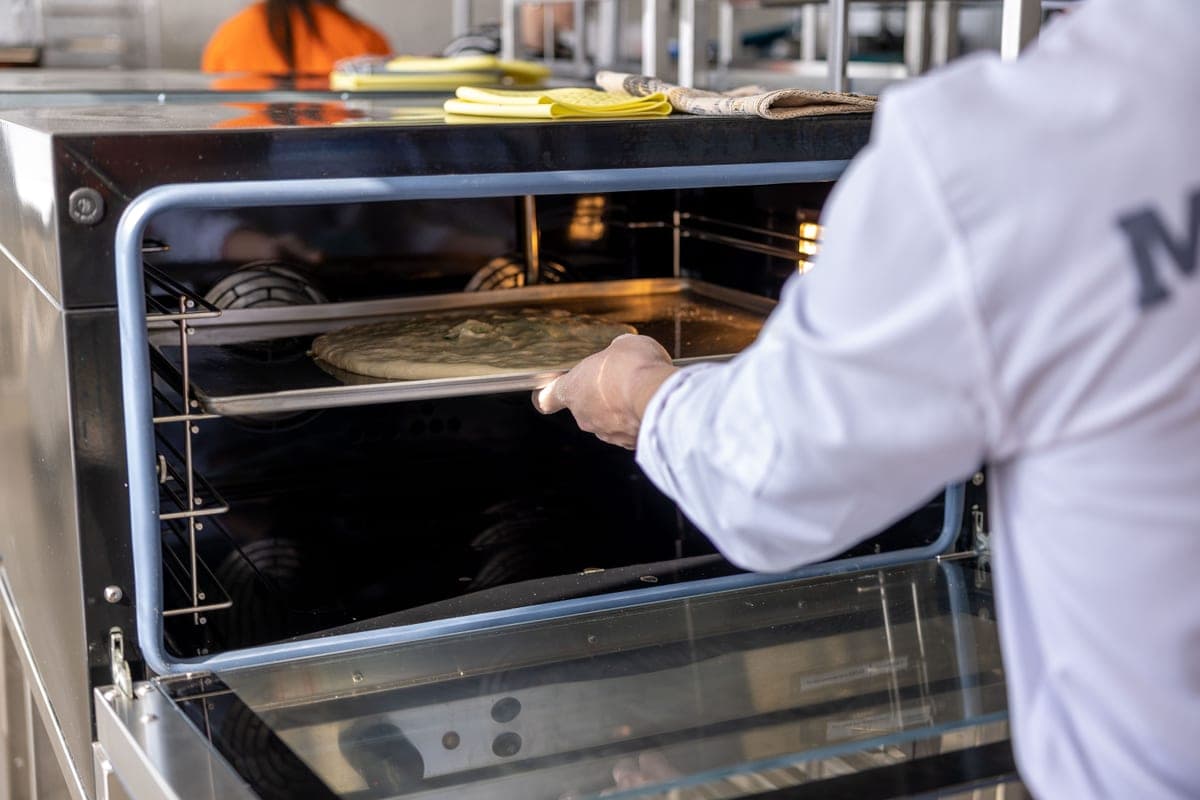 A pizza being placed onto a hot baking surface