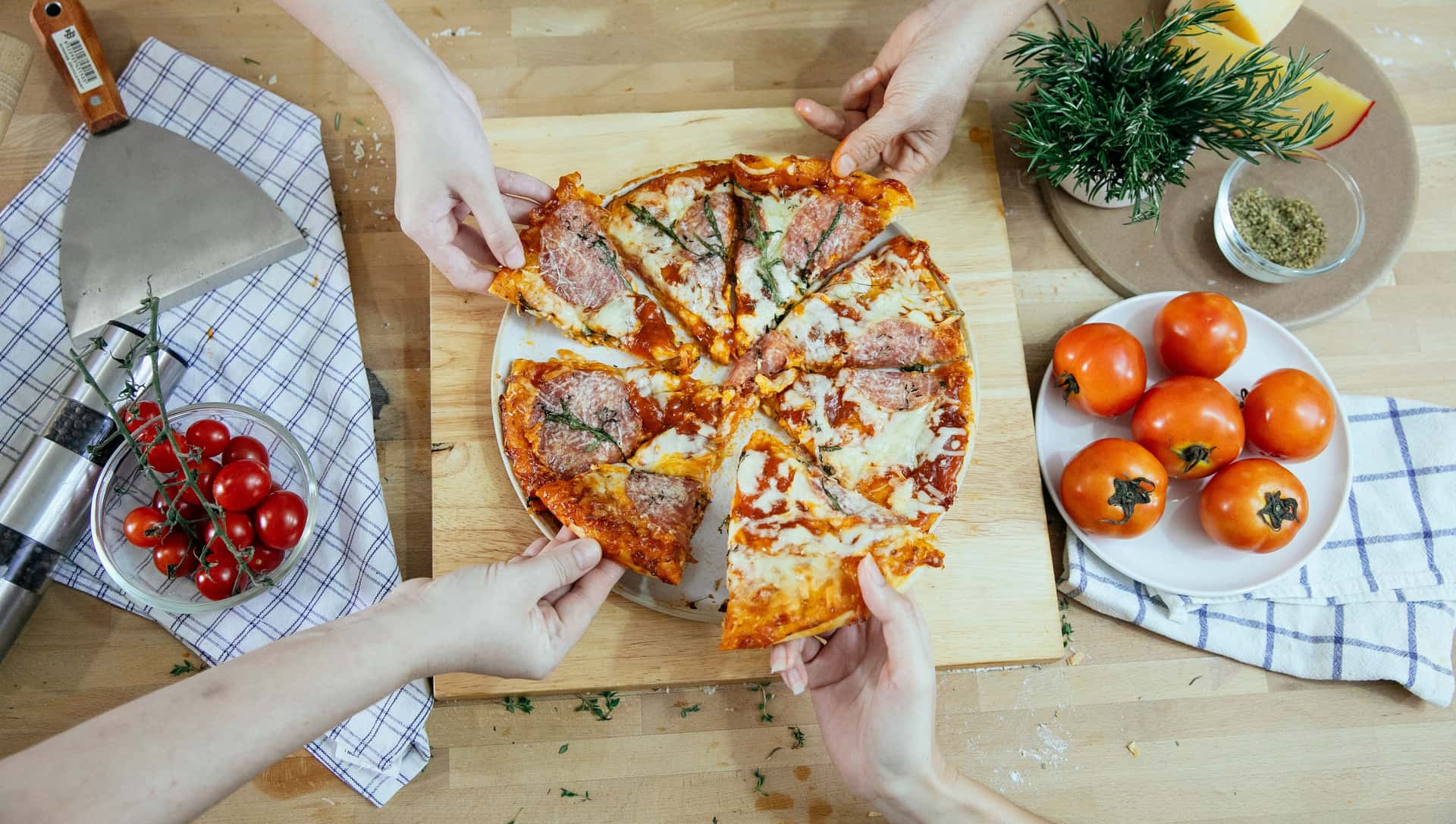 People taking slices from a shared pizza outdoors